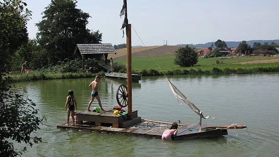 drei Kinder auf Bootsfloß baden im hauseigenen See